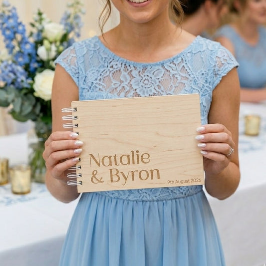 Bridesmaid in a blue dress holding a wooden guest book with 'Natalie & Byron' and date.