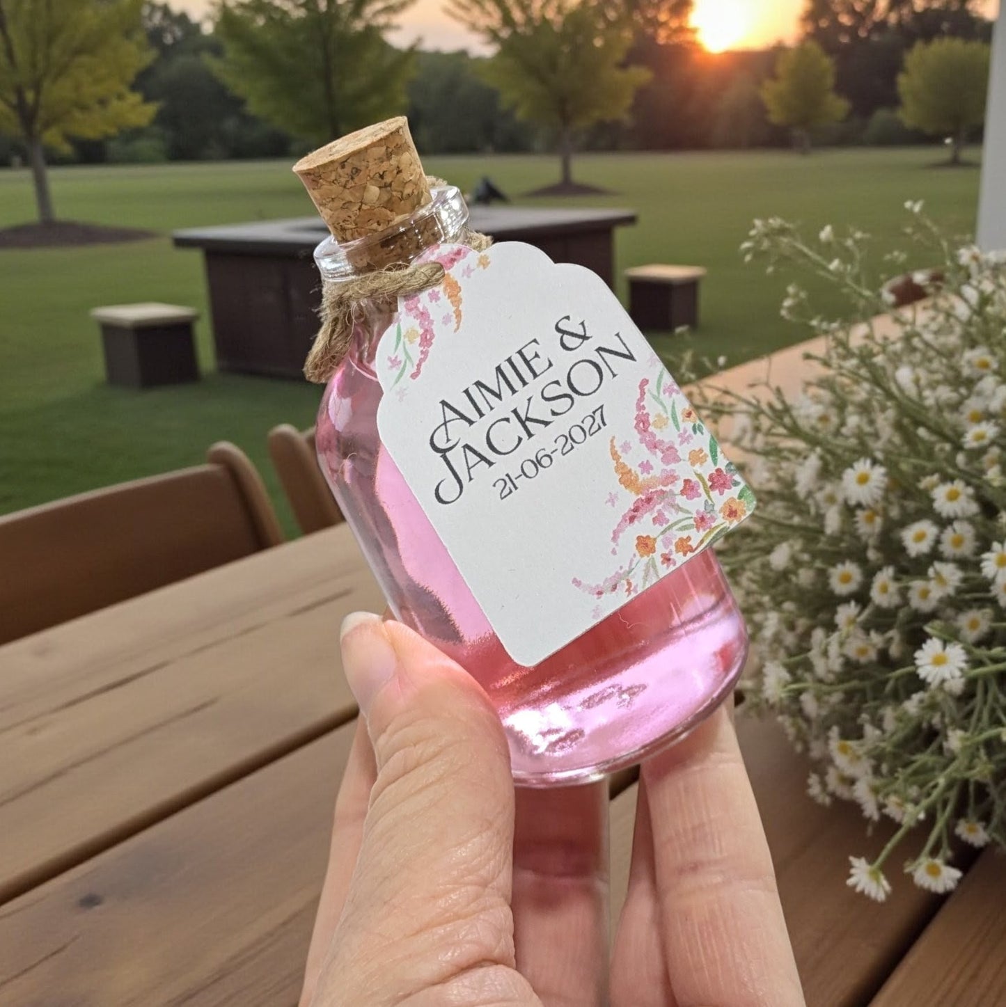 Hand holding a wedding shot bottle with a beautiful custom floral tag with the couples names on it. 
