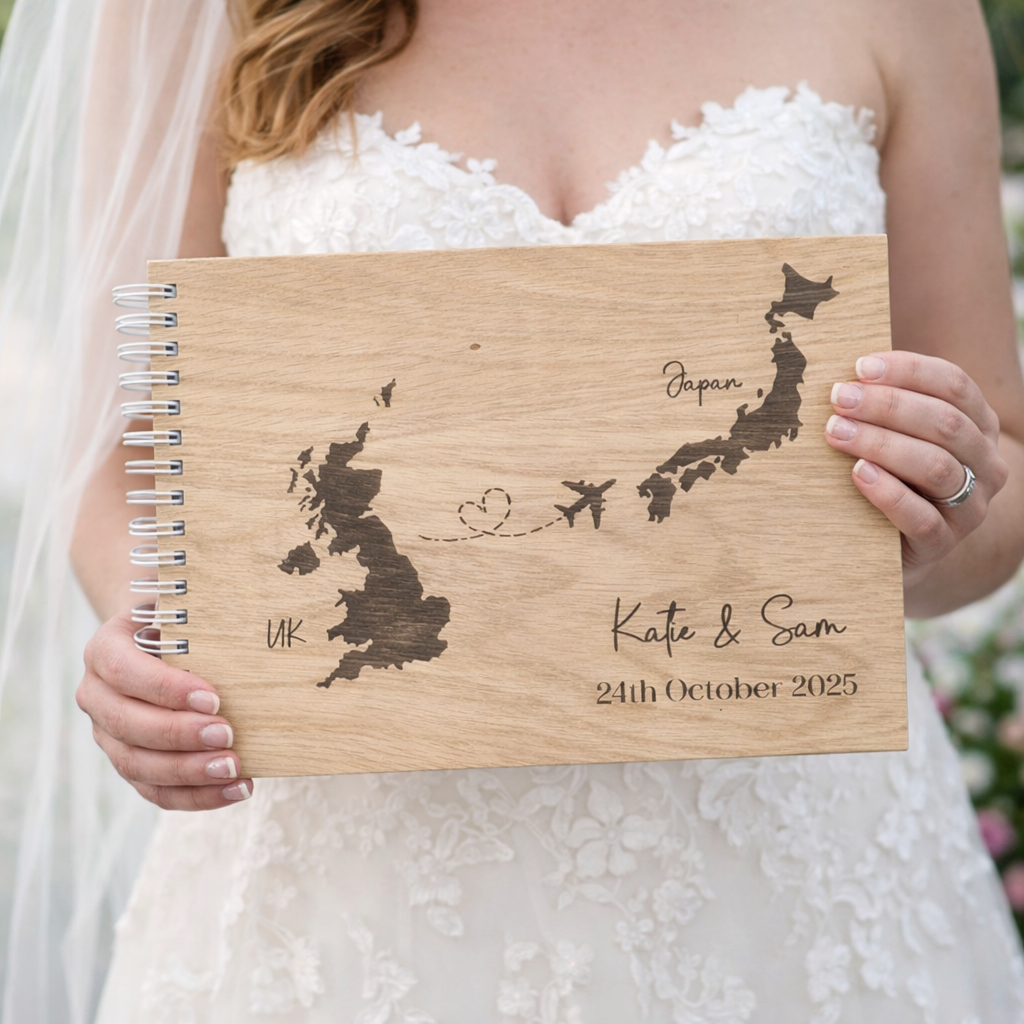 Wooden wedding guest book with engraved map of UK and Japan held by a person in a wedding dress.