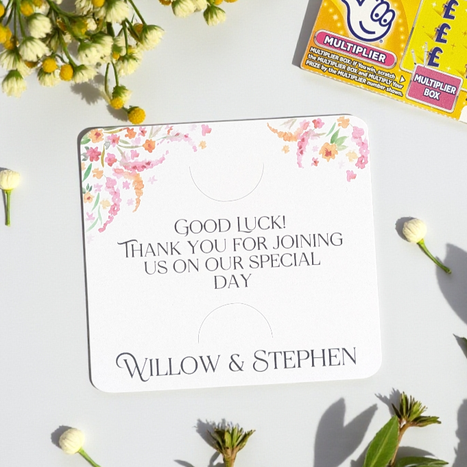 Themed bridgerton wedding favour on a white table with florals in the corner and a scratch card. 