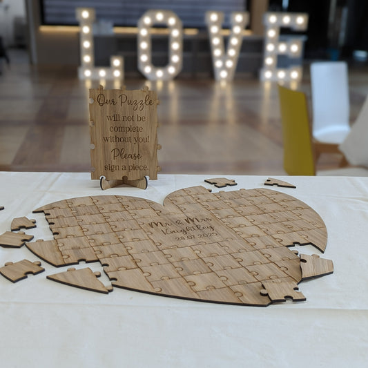 A wooden heart-shaped puzzle guest book with individual interlocking pieces for guest signatures surrounding a large personalized center.