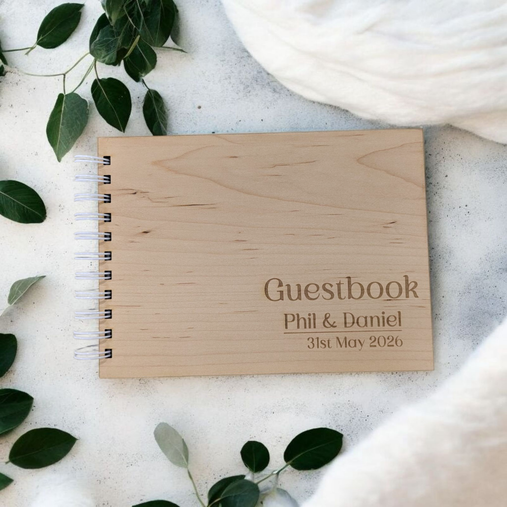 Engraved wood wedding guest book on a concrete worktop with leaves around the wedding book.