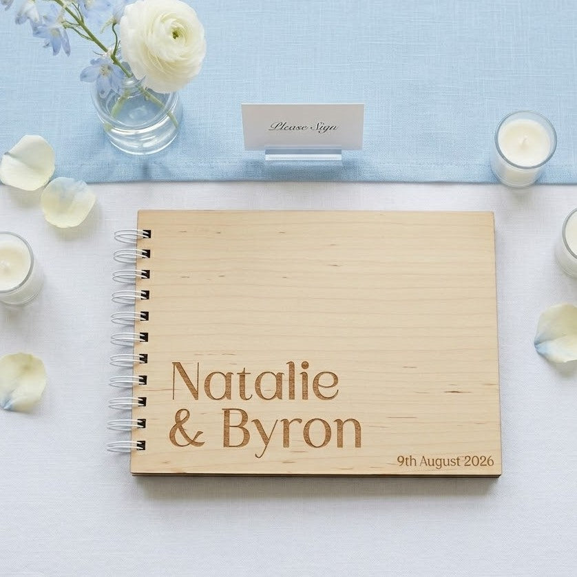 Wooden wedding guest book with engraved names and date on a decorative table with flowers and candles.