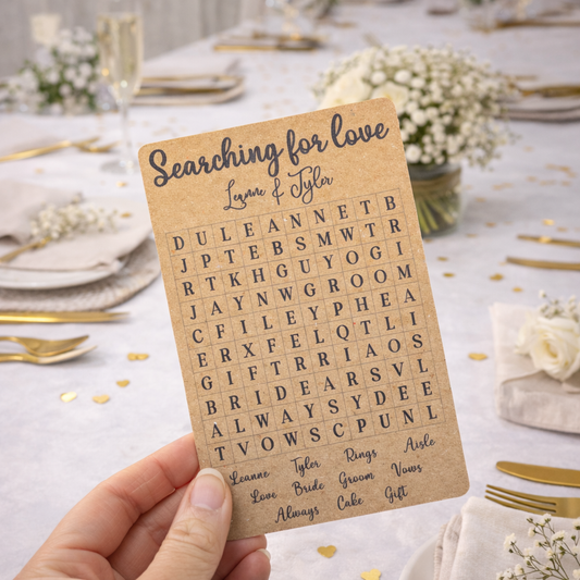 Hand holding a wedding word search card on a decorated table with flowers and plates.