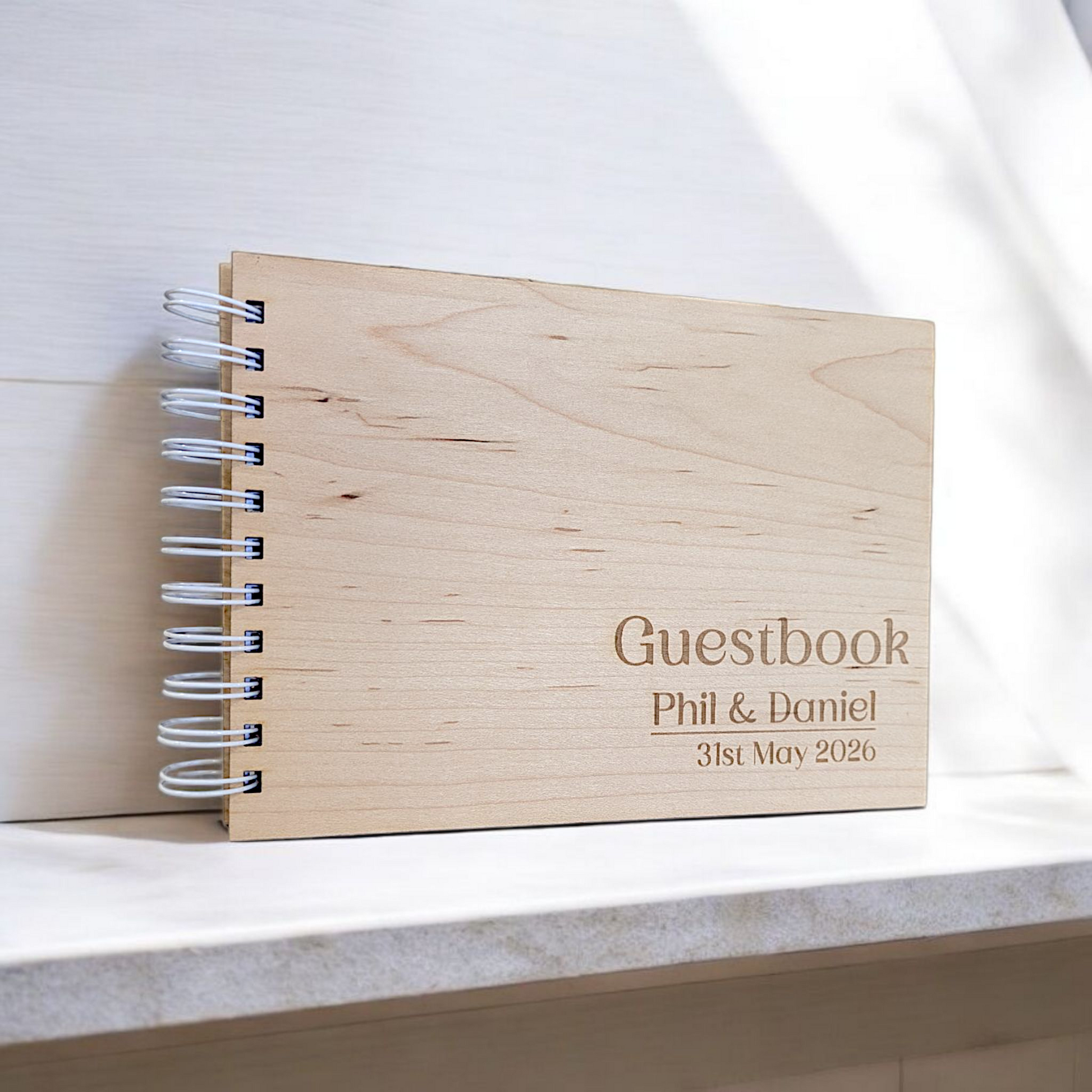 A wooden wedding guestbook with engraved names and a date, lying on a marble surface.