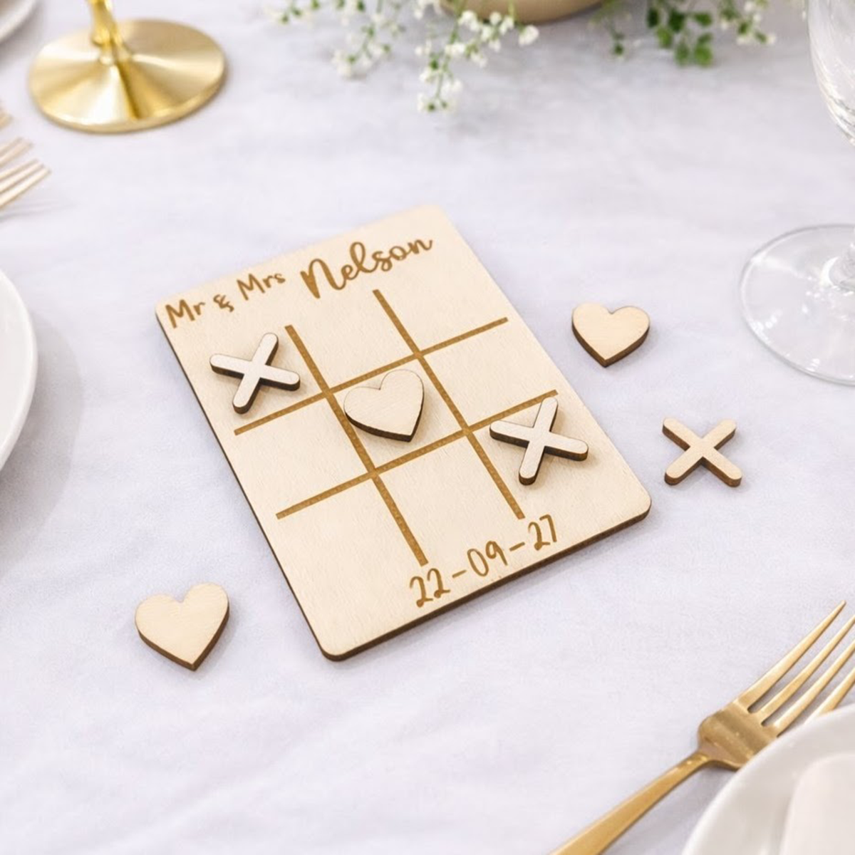 Wooden wedding table game that is a noughts and crosses board with personalised names and date being given as wedding favours on a table setting.