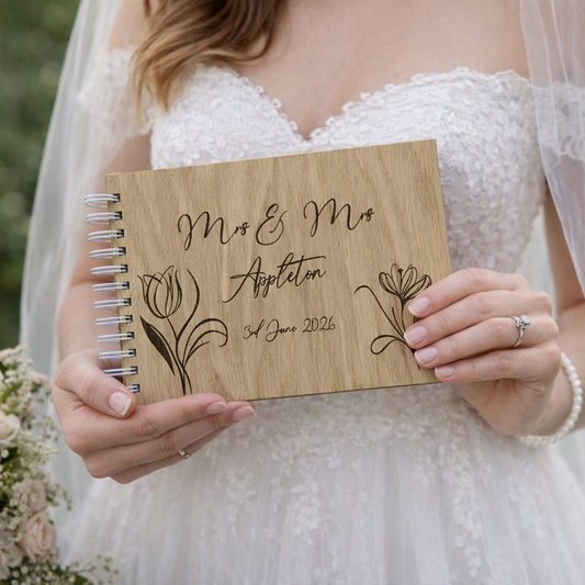 Bride holding a wooden wedding guest book with engraved text and floral designs.