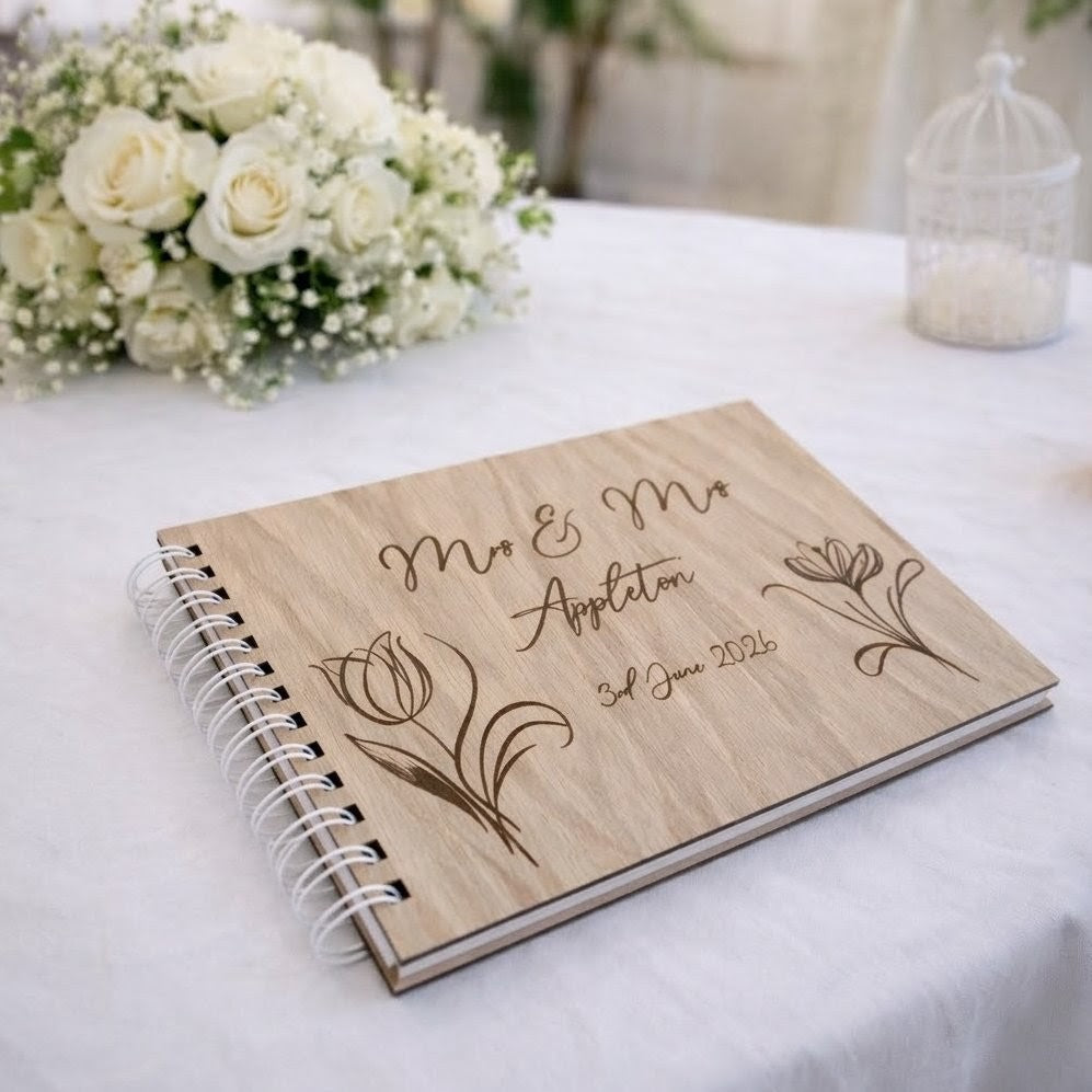 Personalised wedding guest book made from oak wood on a white table with floral bouquet on the table.
