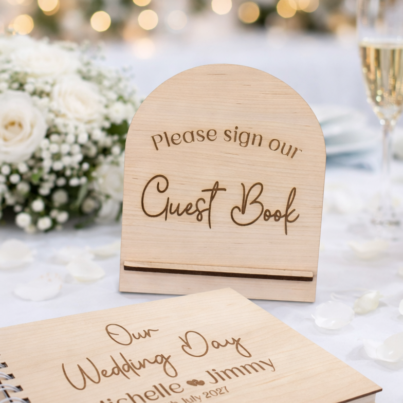 Engraved wooden wedding guest book sign on a wedding table with a guest book and bouquet