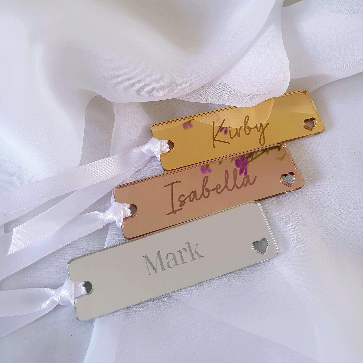 Three customised bookmarks with engraved names. Each acrylic bookmark is tied with white ribbon