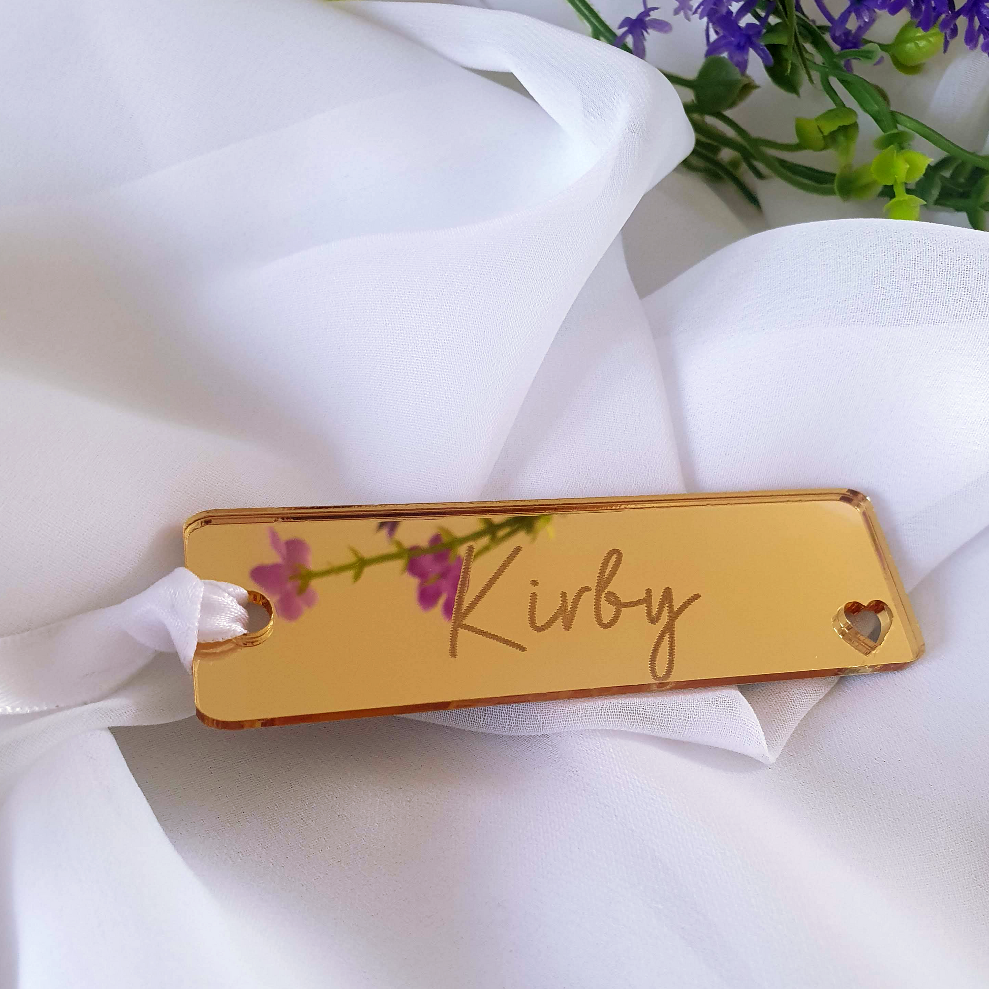 Gold acrylic bookmark with a personalized engraving of a name. The corner of the bookmark has a heart shaped cutout  