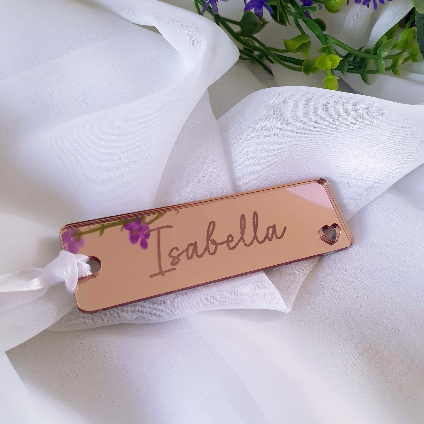 Rose gold mirrored acrylic bookmark with a custom engraving of a the name 'Isabella'. The bookmark gift is tied with white ribbon